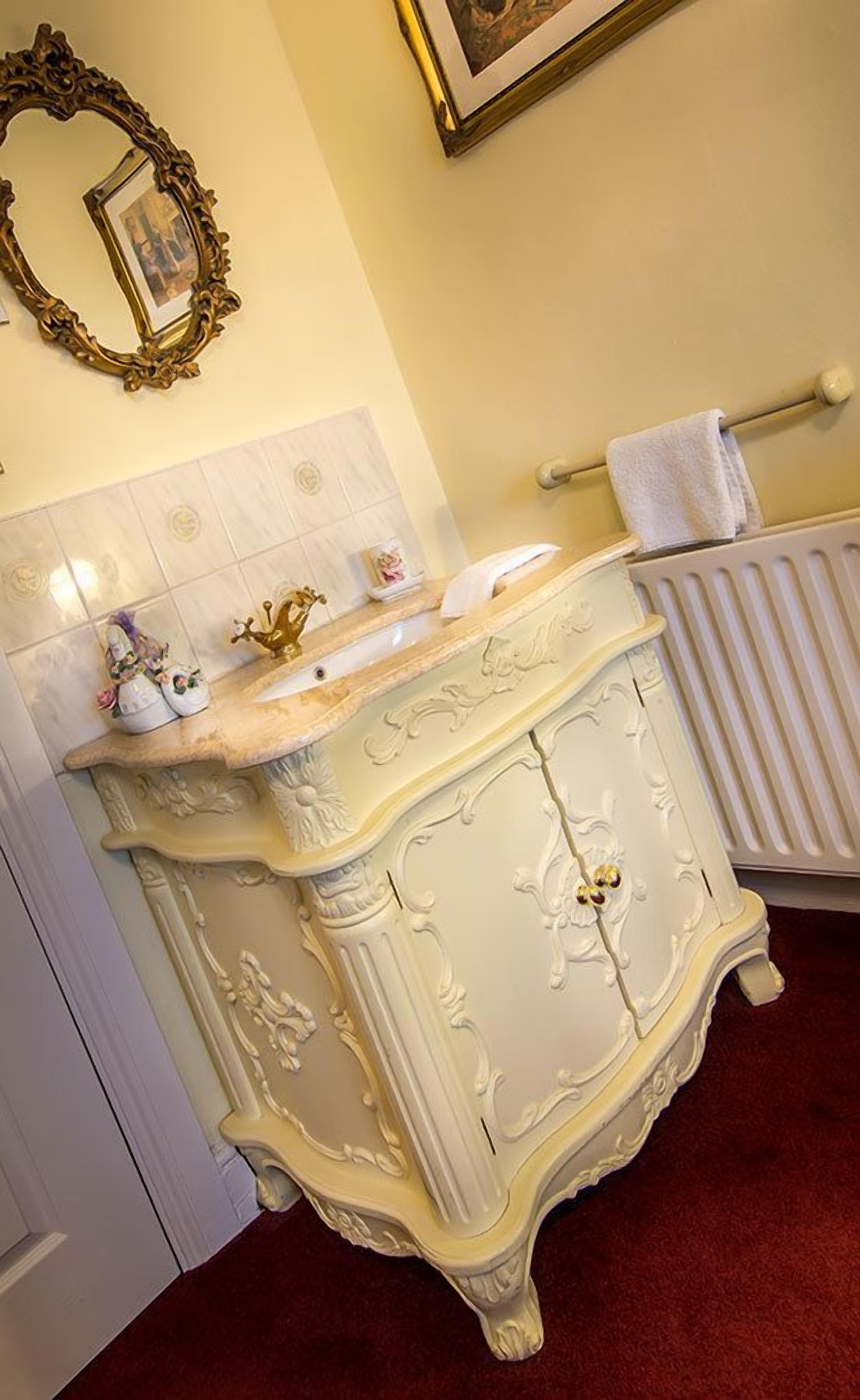 A bathroom with a white vanity, a gold-framed mirror, and a towel rack.