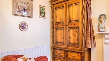 Una stanza con un divano in velluto rosso, un armadietto in legno e un termosifone.