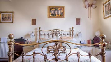 Ein Schlafzimmer mit einem klassischen Himmelbett, einem Heizkörper, einer Kommode und einer Wandlampe.