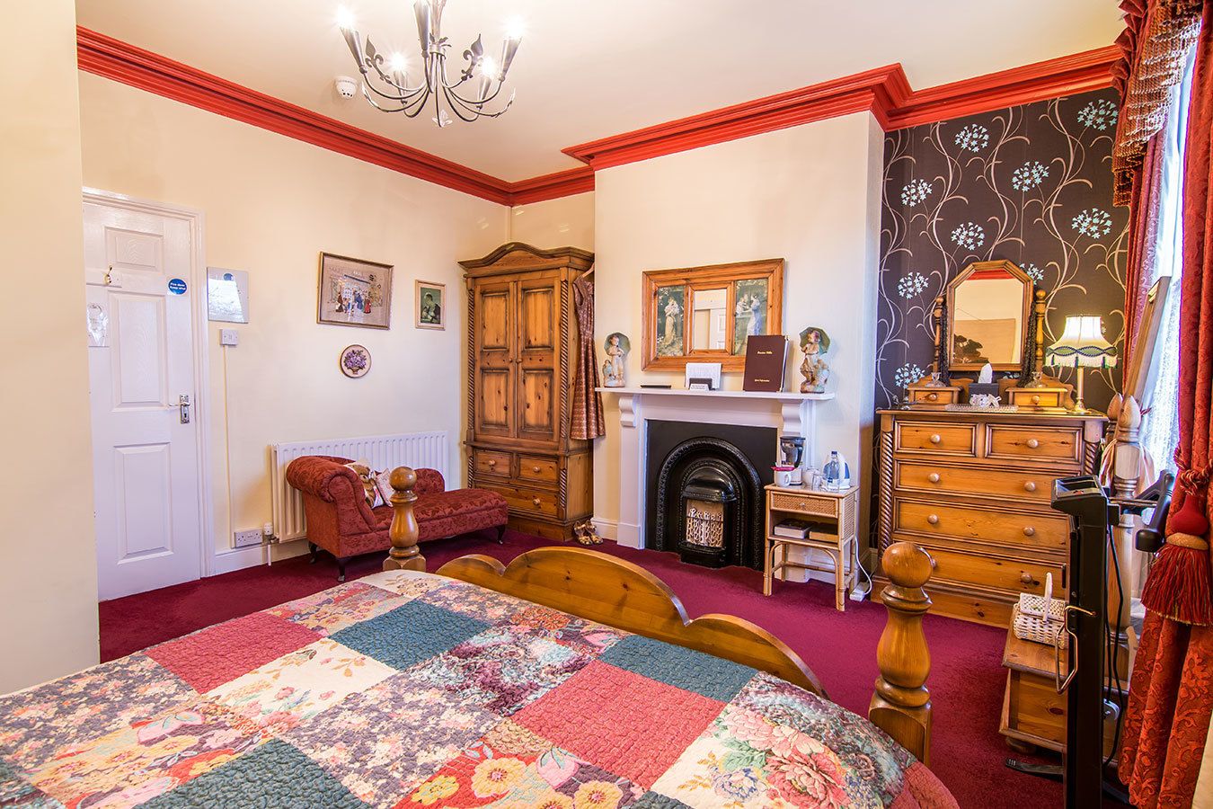 A bedroom with a large bed, a fireplace, wooden furniture, and a chandelier.