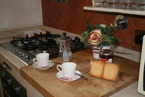 A kitchen counter with a gas stove, a coffee maker, a cup, a jar of jam, and two slices of bread.