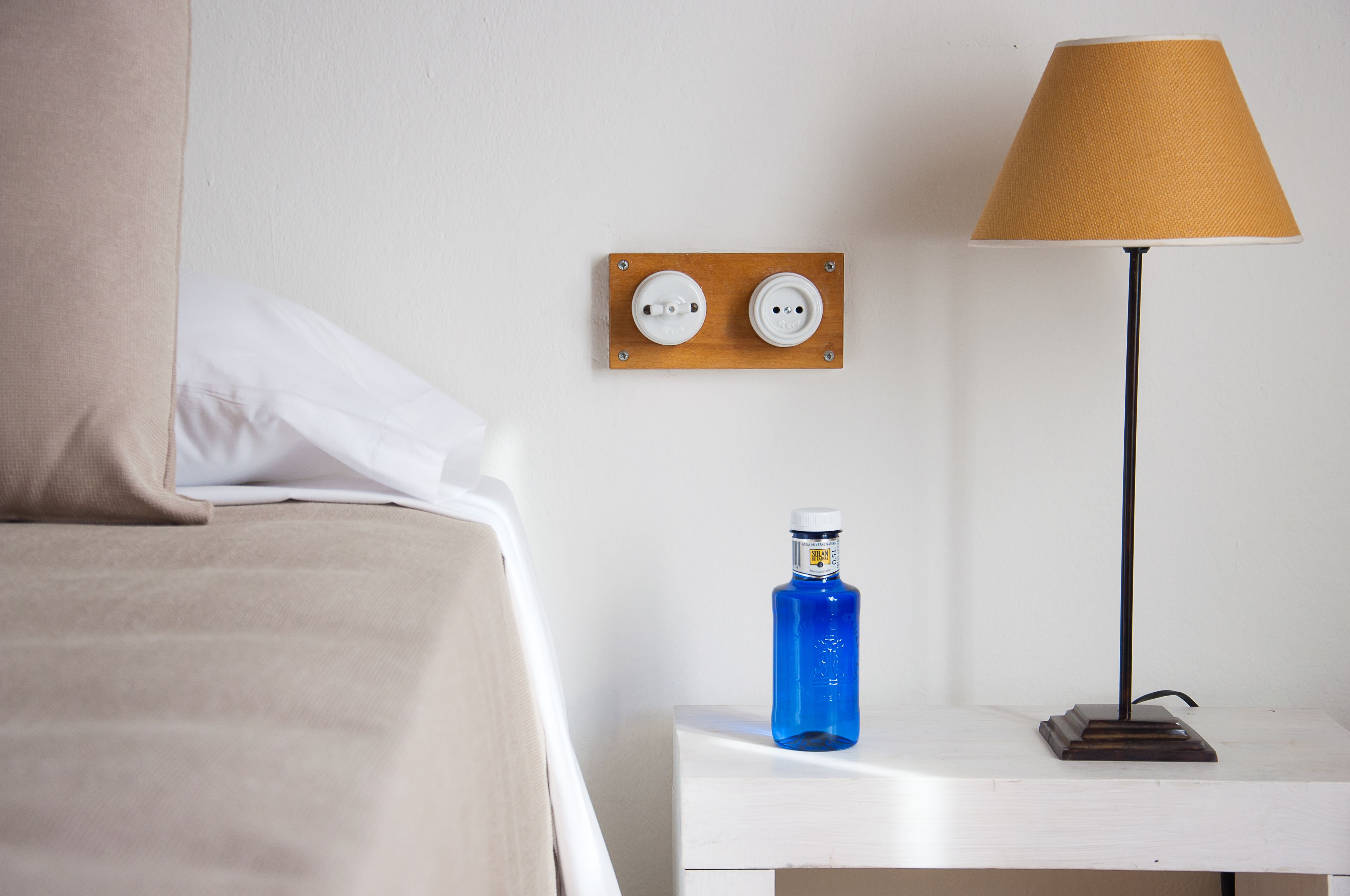 A hotel room with a bed, a nightstand, a lamp, and a wall socket.