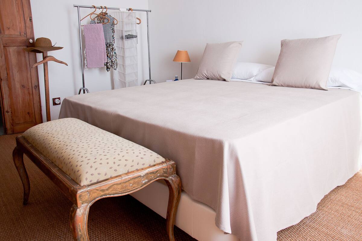 A neatly made bed with a large pillow, a bedside lamp, and a wooden bench.