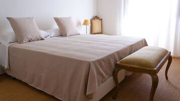 Una cama bien hecha con un banco a juego, una lámpara de noche y un espejo en la pared.