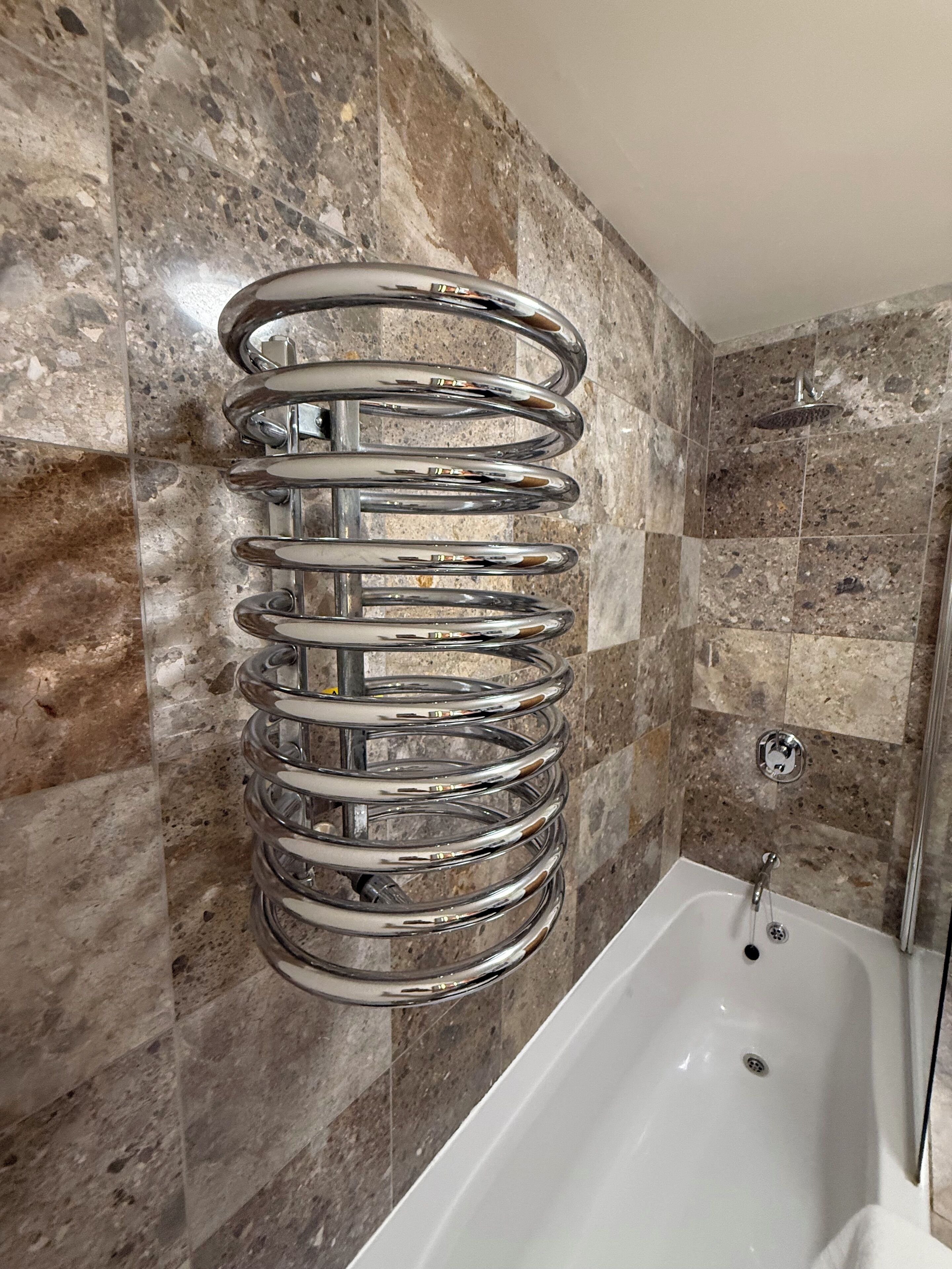 Ein Badezimmer mit Marmorwand, einem chromfarbenen Handtuchhalter und einer weißen Badewanne.