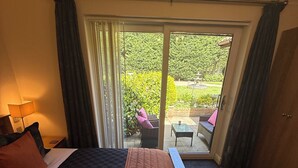 Hotelkamer met een bed, een klein tafeltje, een stoel en uitzicht op een tuin door een schuifdeur.