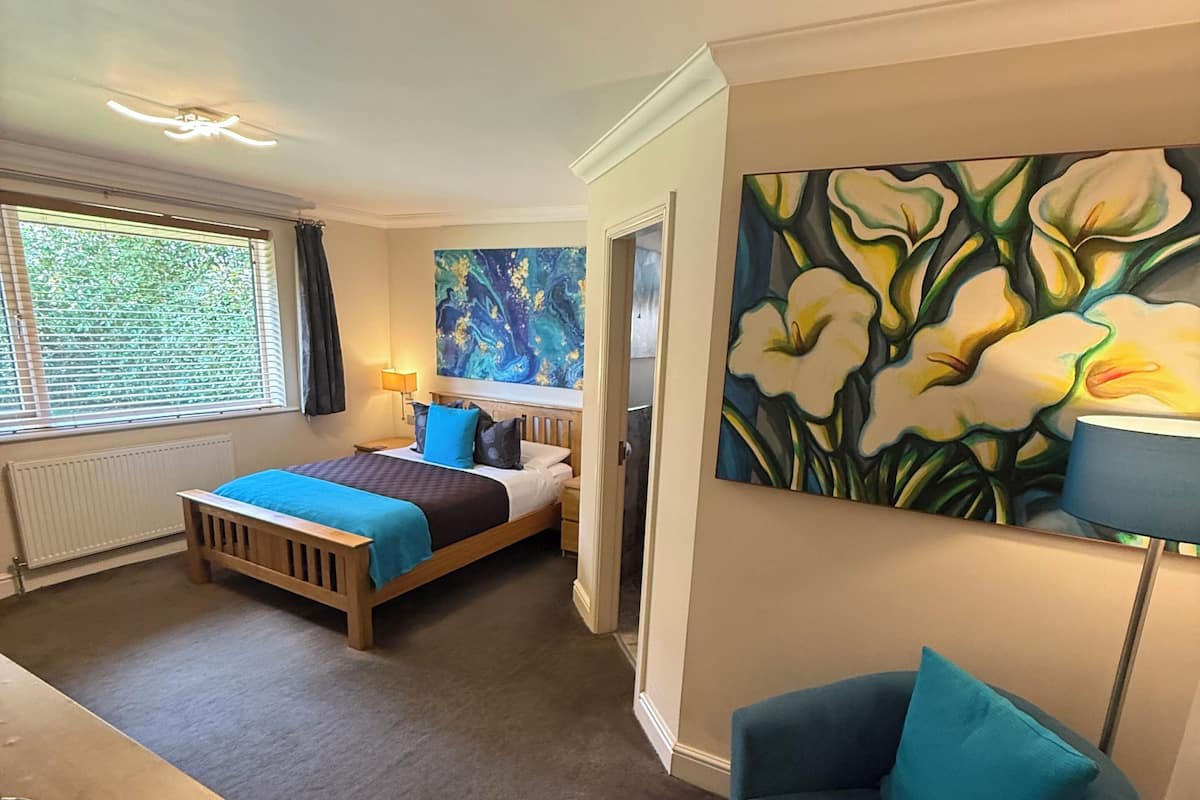 Een hotelkamer met een bed, een bureau, een stoel en een groot bloemen schilderij aan de muur.