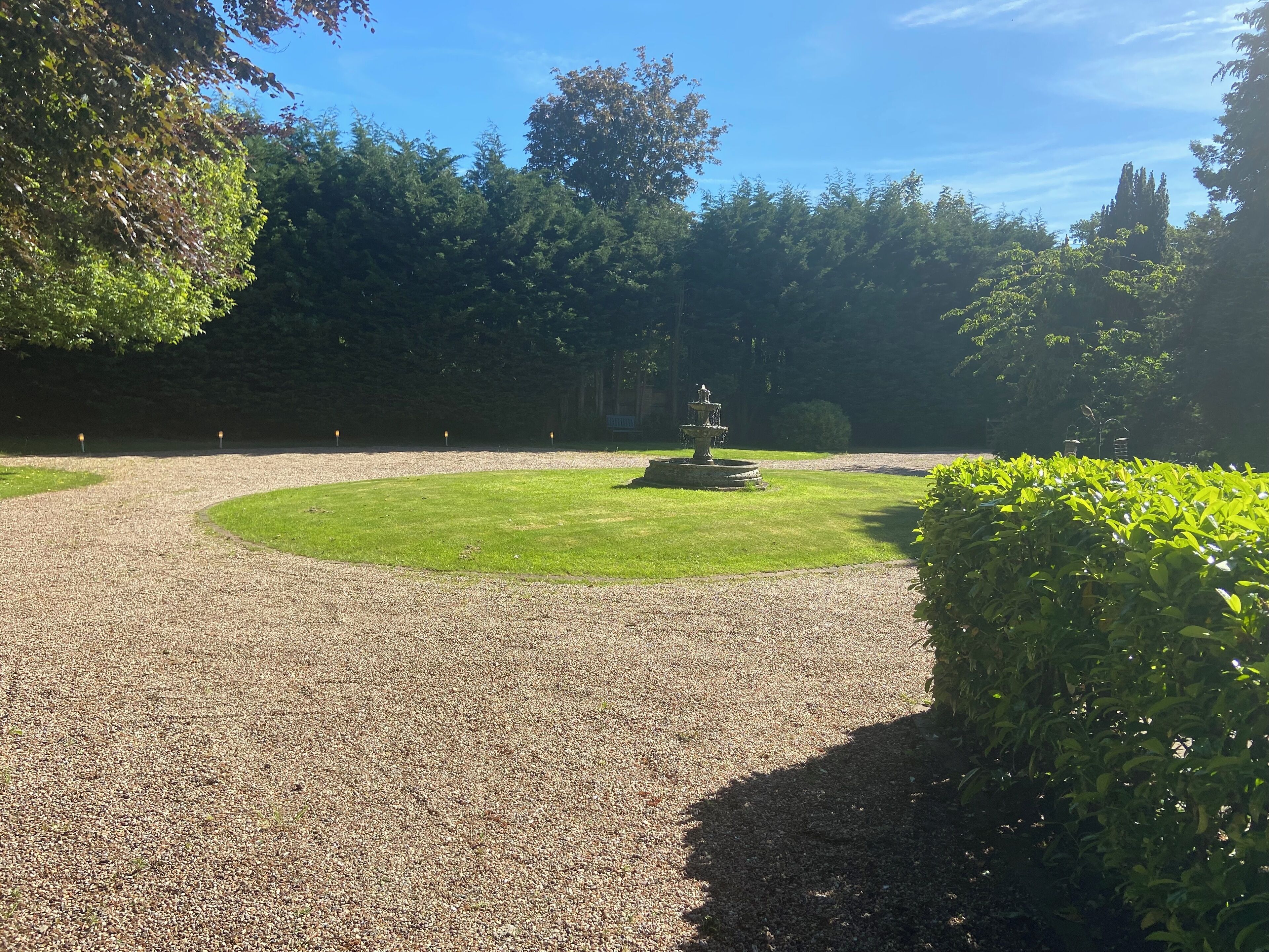 A gravel pathway leading to a fountain in a park.