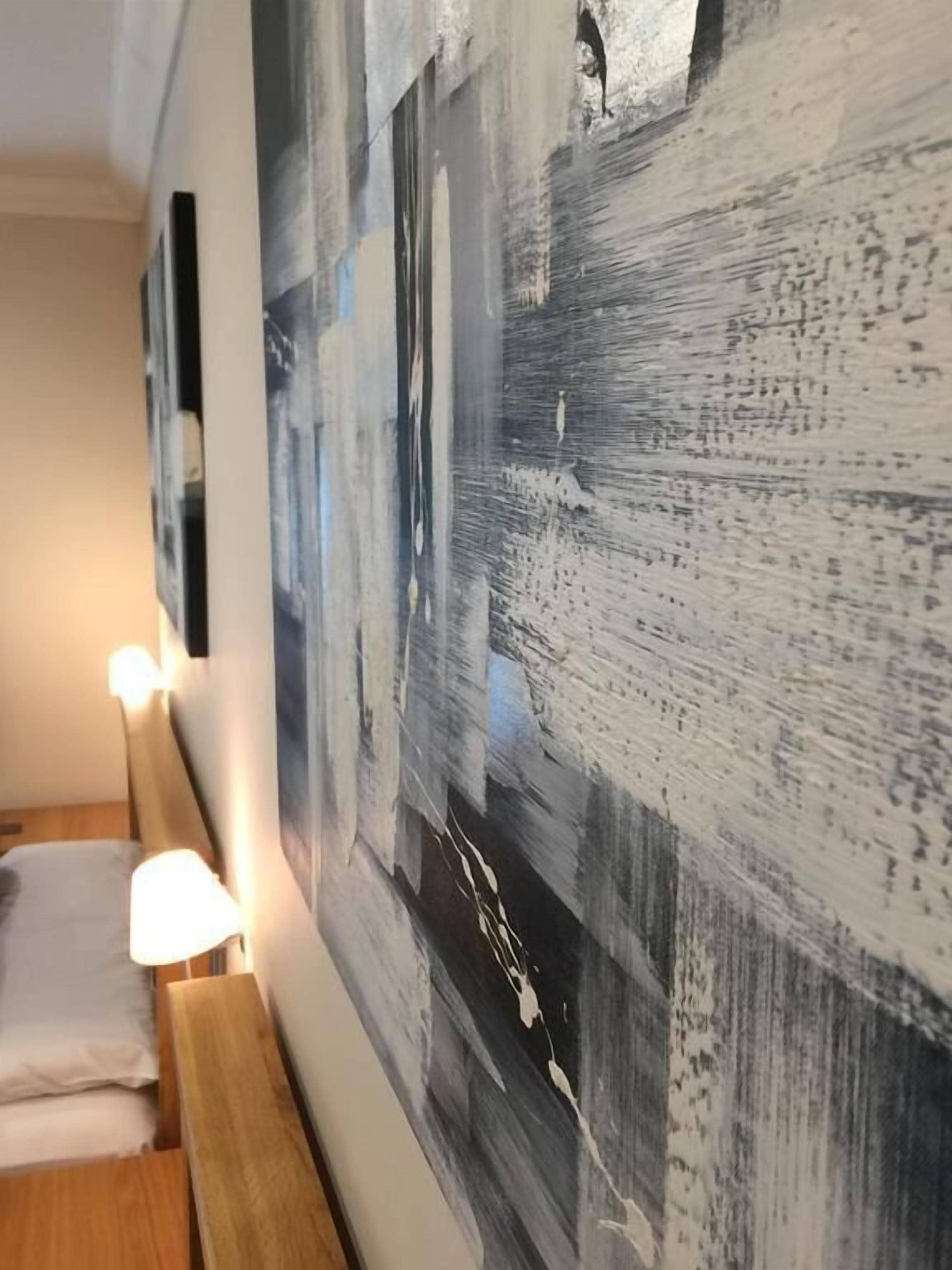 A hotel room with a large abstract painting on the wall, a wooden headboard, and a bedside lamp.