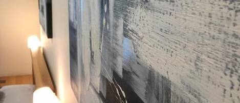 A hotel room with a large abstract painting on the wall, a wooden headboard, and a bedside lamp.