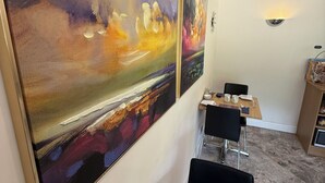 Een eetgedeelte met een tafel gedekt voor twee personen, een menukaart en een schilderij aan de muur.