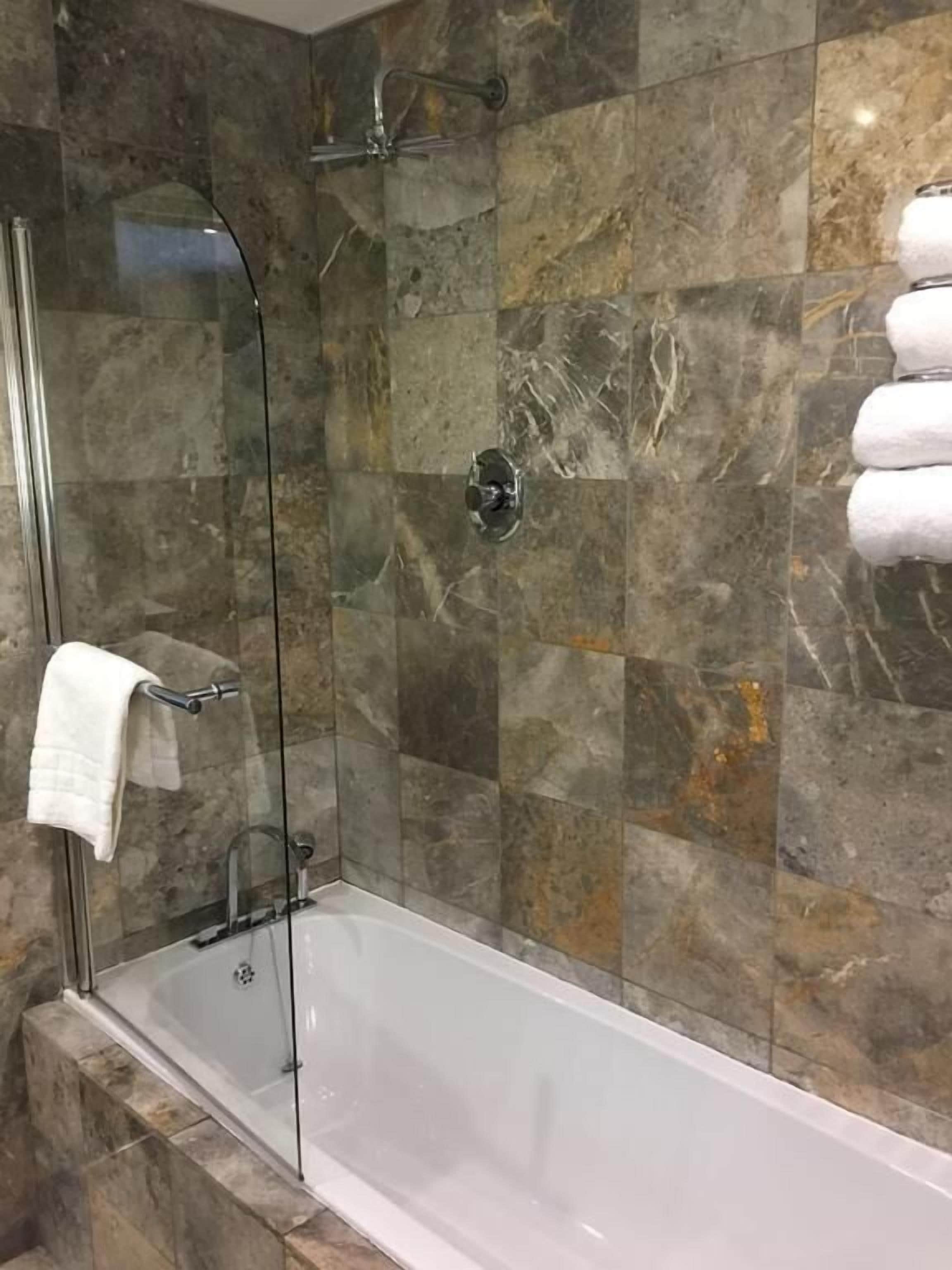 A modern bathroom with a glass-enclosed shower, a white bathtub, and marble tiles.