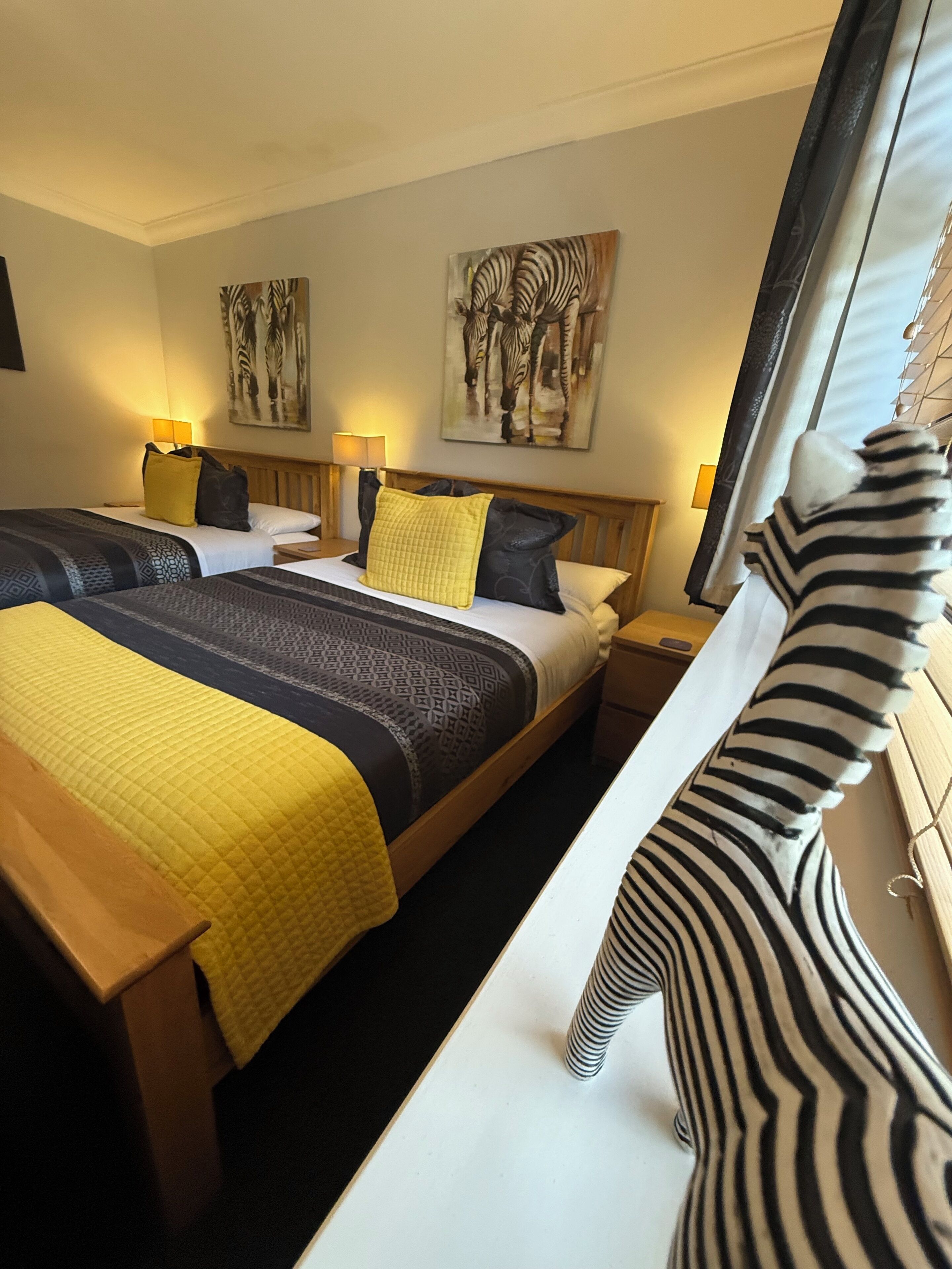 A hotel room with two beds, a zebra-patterned pillow, and zebra-themed artwork on the walls.