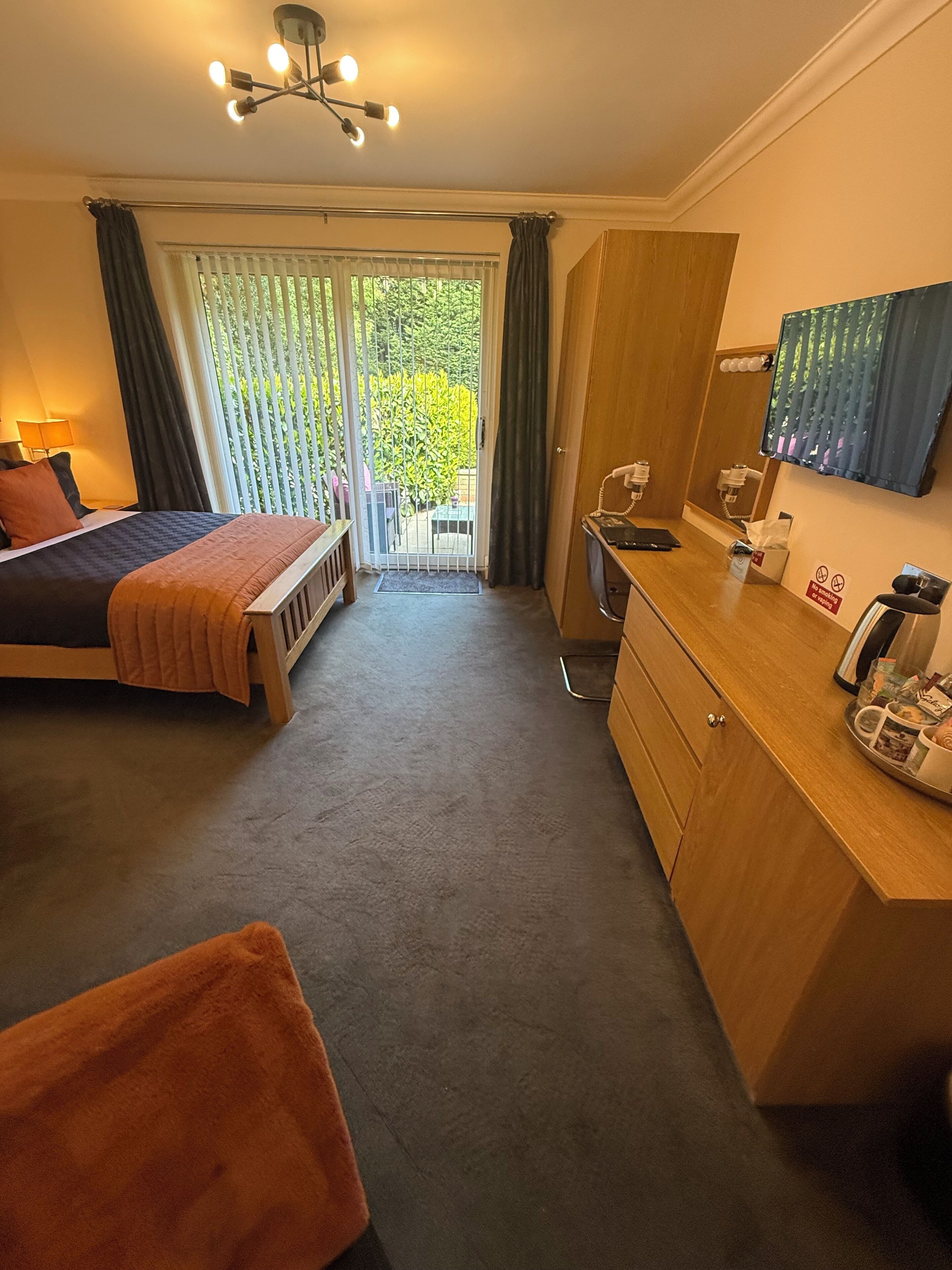 Habitación de hotel con cama, escritorio, silla, una kitchenette pequeña y un ventanal corredero que da a un balcón.
