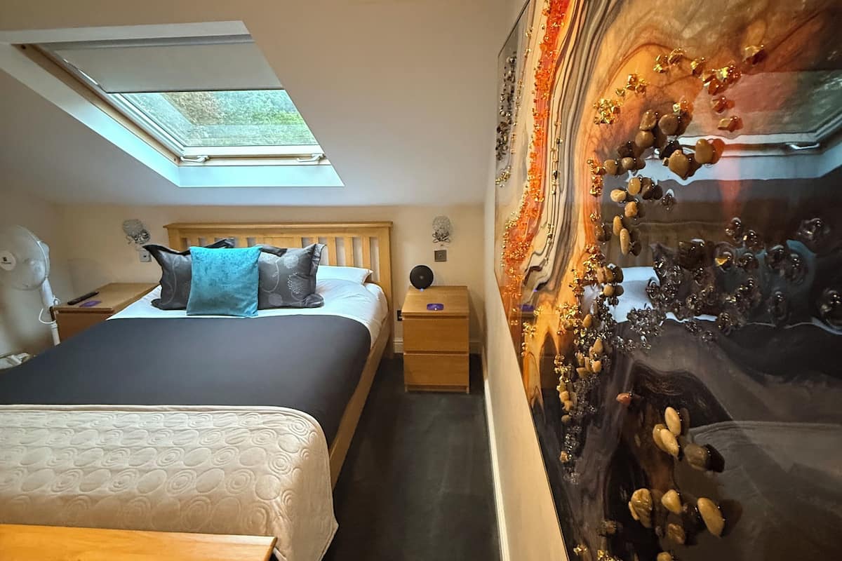 Een slaapkamer met een bed, een nachtkastje, een kunstwerk aan de muur en een dakraam.