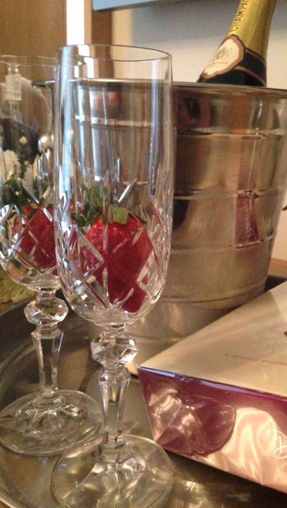 Dos copas de cristal sobre una bandeja con una botella de champán y un cuenco de metal al fondo.