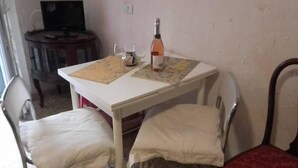 Una habitación pequeña con una mesa blanca, dos sillas blancas, una botella de vino y un televisor al fondo.