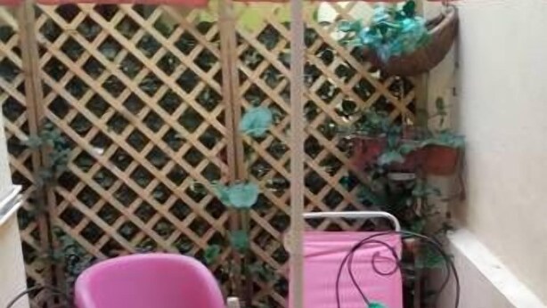 Un pequeño patio al aire libre con una mesa, sillas y una sombrilla blanca. Una de las sillas es rosa.