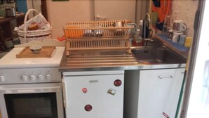 Una cocina con estufa, horno y refrigerador. Se observa un escurreplatos, un lavamanos y diferentes utensilios de cocina sobre las encimeras.