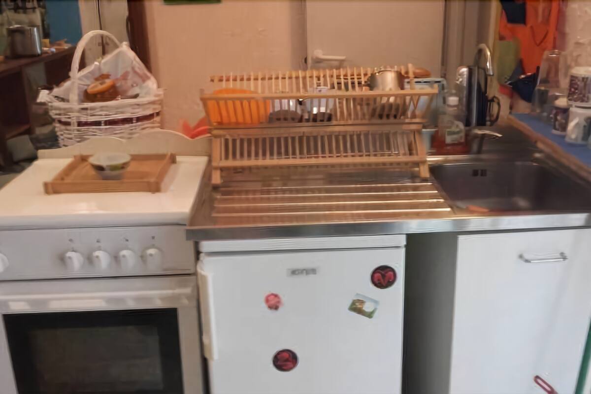 A kitchen with a stove, oven, and refrigerator. There is a dish rack, a sink, and various kitchen items on the countertops.