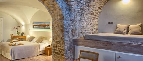 A bedroom with a stone wall, a bed, a desk, and a chair.