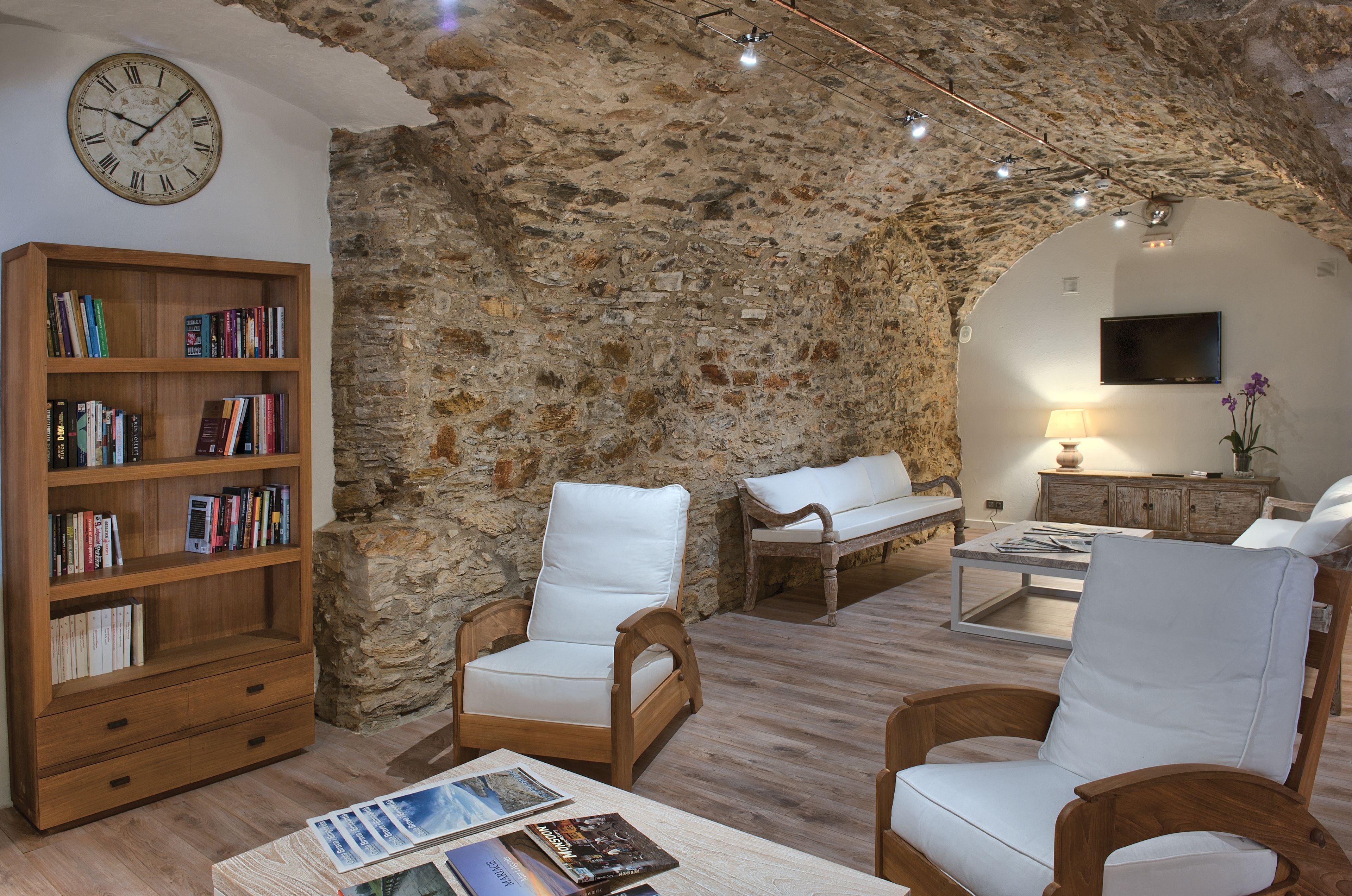 Un salon chaleureux avec un mur en pierre, des meubles en bois, une bibliothèque et un téléviseur à écran plat.