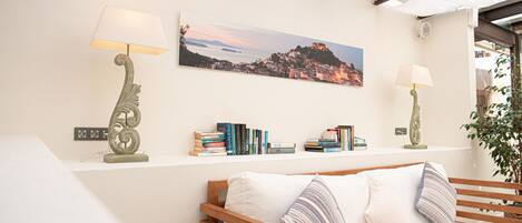 Una habitación acogedora con un banco de madera, un estante con libros y una pintura de paisaje.