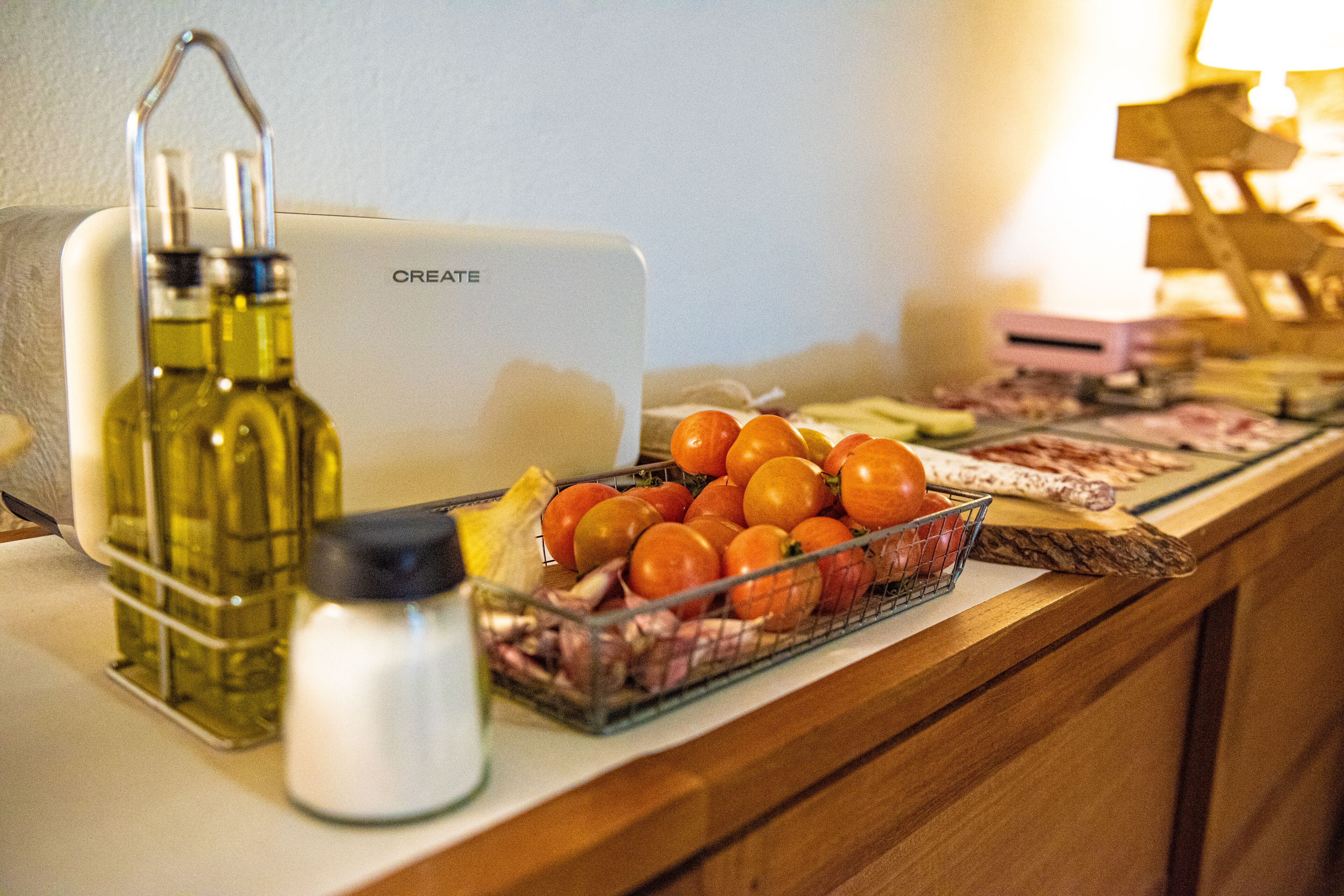 A kitchen counter with a white appliance, a glass bottle, a metal container, and a basket of tomatoes.