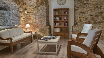 Un salón acogedor con una pared de piedra, una estantería de madera, un sofá blanco y dos sillones de madera.
