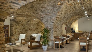 A restaurant with stone walls, wooden furniture, and a central plant. - Hotel el Petit Convent (Begur)