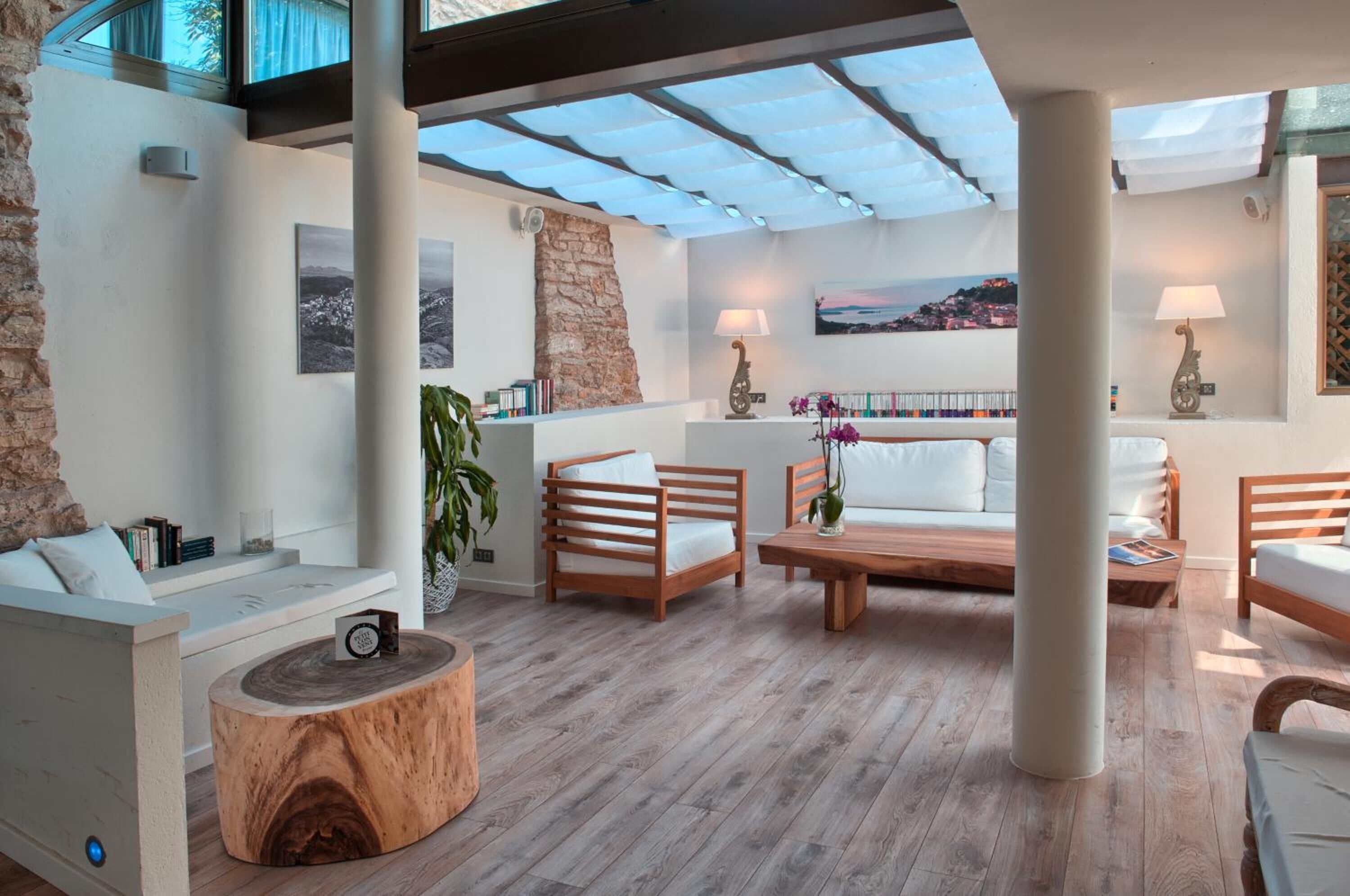 Ampla sala de estar com piso de madeira, mobiliário branco, parede com detalhes em pedra e vista para uma cidade costeira.