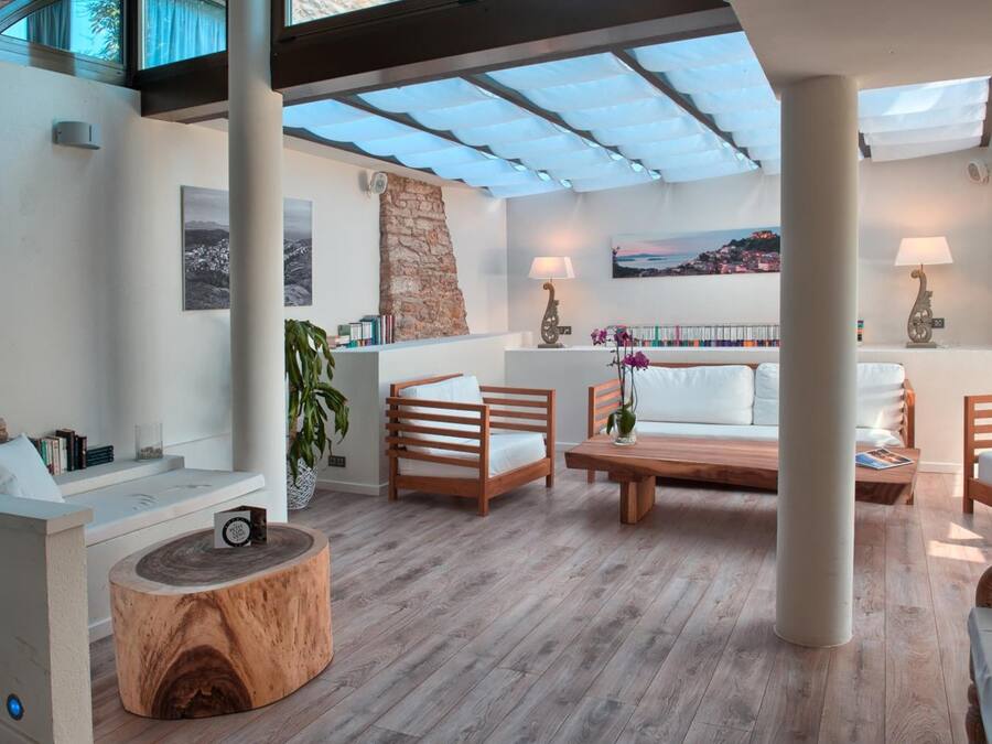 Ampla sala de estar com piso de madeira, mobiliário branco, parede com detalhes em pedra e vista para uma cidade costeira.