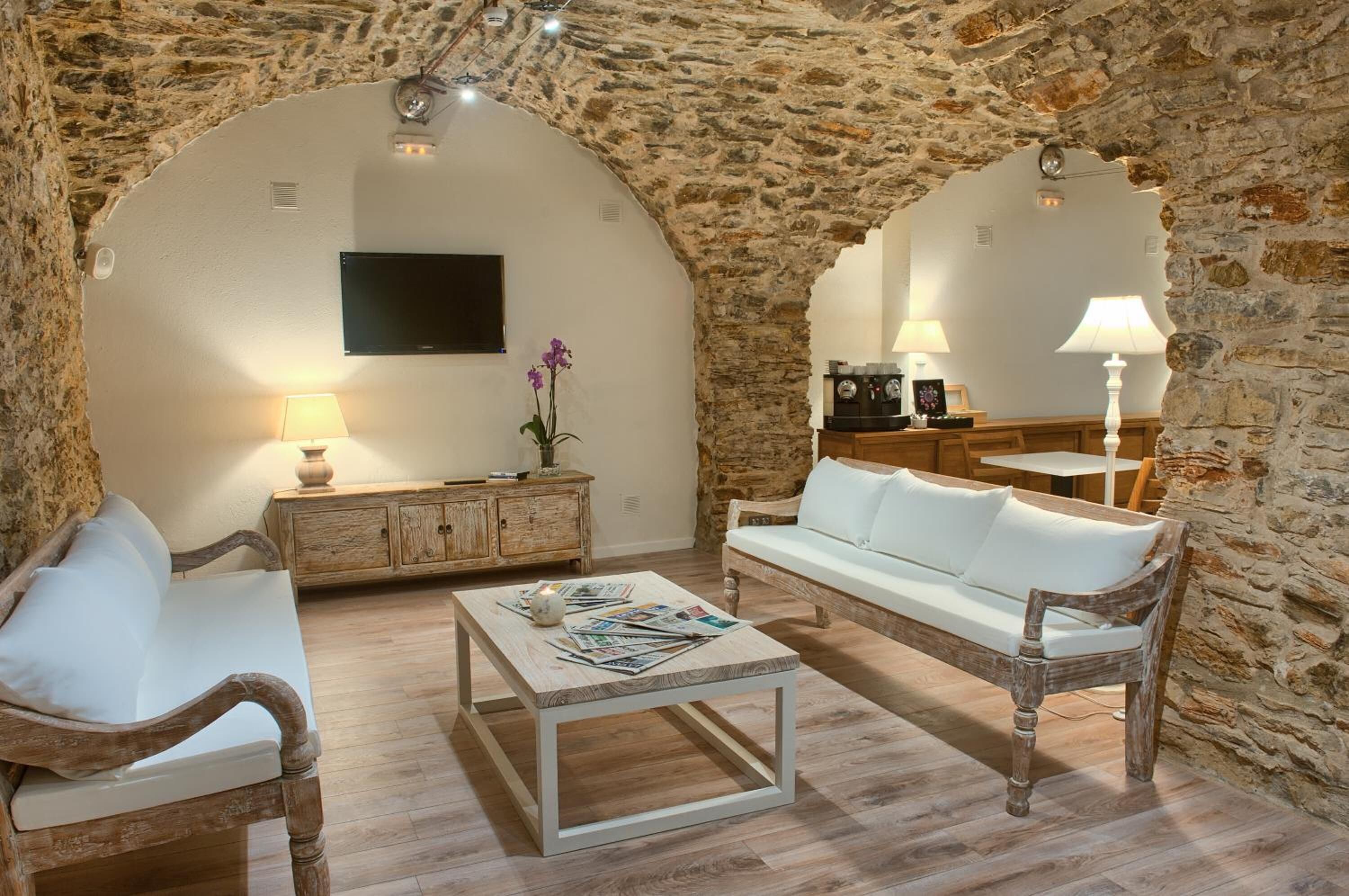 A cozy living room with stone walls, a white sofa, a wooden coffee table, and a television mounted on the wall.