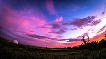 A panoramic view of a landscape with a field and trees under a colorful sky.