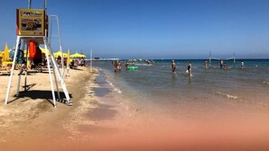 A beach with a lifeguard stand, umbrellas, and people in the water. - Hotel Caravan (Pesaro)