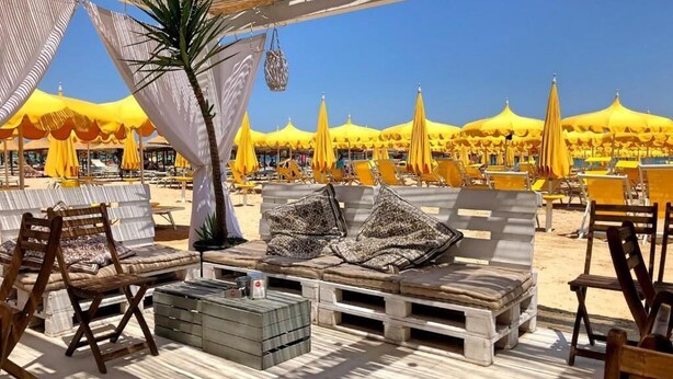 A beachside lounge with wooden furniture, yellow umbrellas, and a clear blue sky. - Hotel Caravan (Pesaro)