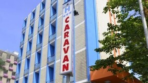 A modern hotel with a prominent 'CARAVAN' sign, featuring a blue and white facade, a covered entrance, and potted plants around the entrance. - Hotel Caravan (Pesaro)