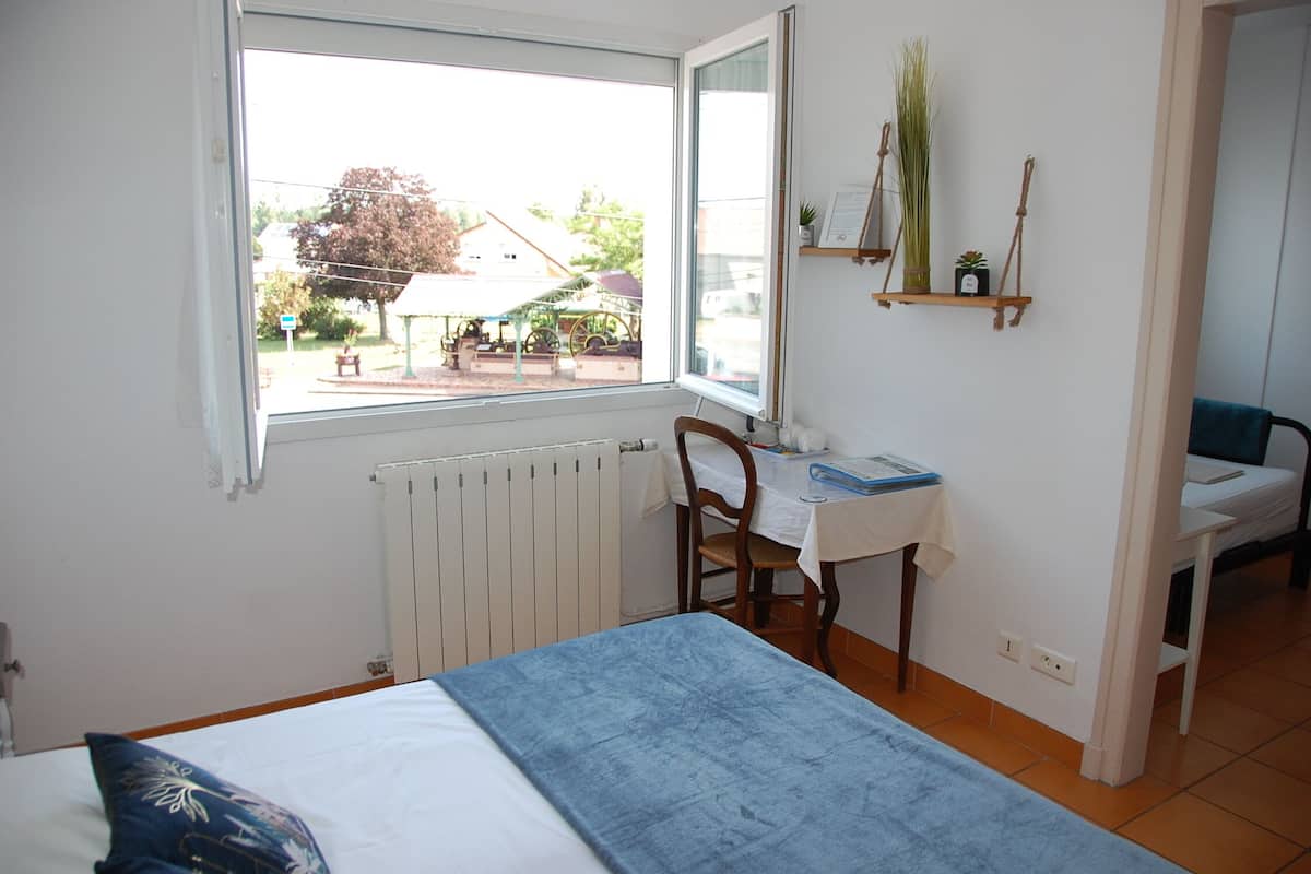 Quarto com cama, escrivaninha, cadeira e janela com vista para a rua.