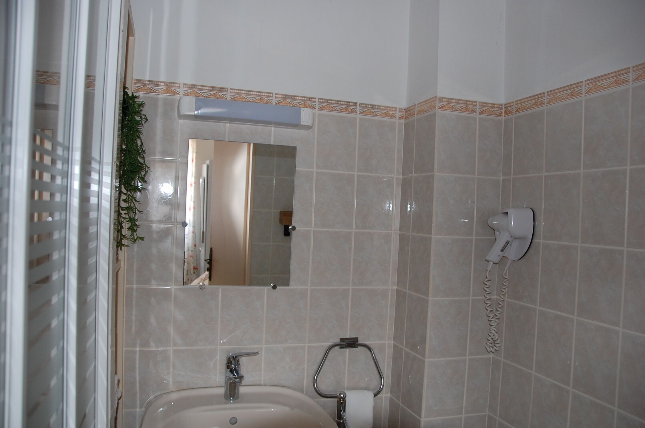 A bathroom with a sink, mirror, and a hairdryer mounted on the wall.