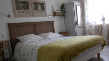 Une chambre à coucher avec une tête de lit en bois, un lit avec une literie blanche et un plaid vert, une table de chevet, une commode et un miroir.