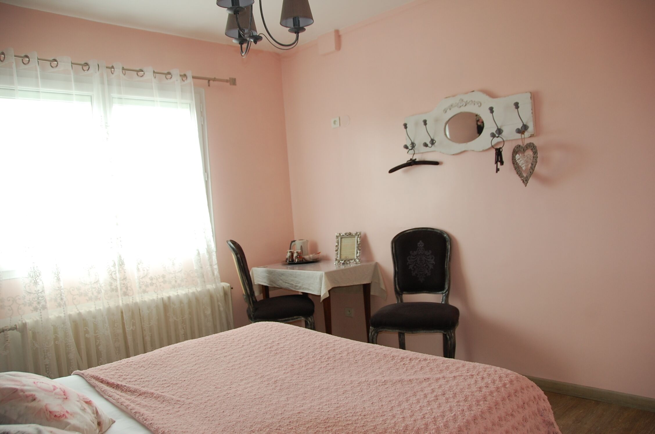 Un dormitorio con cama, una mesa con sillas, una ventana con cortinas y adornos en la pared.