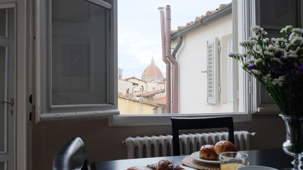 Una mesa de desayuno con cruasanes, un vaso de jugo de naranja y vista a un edificio con forma de cúpula a través de una ventana.