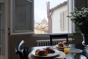 A breakfast table with croissants, a glass of orange juice, and a view of a dome-shaped building through a window. - Vivaldi Terrace (Florence)