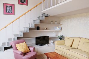 A living room with a staircase, a television, a pink armchair, a beige sofa, and a wooden coffee table.