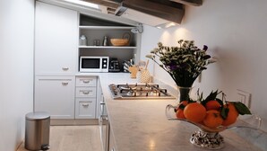 Una cocina moderna con armarios blancos, un cubo de basura de acero inoxidable, una estufa a gas y un florero con flores y naranjas en la encimera.