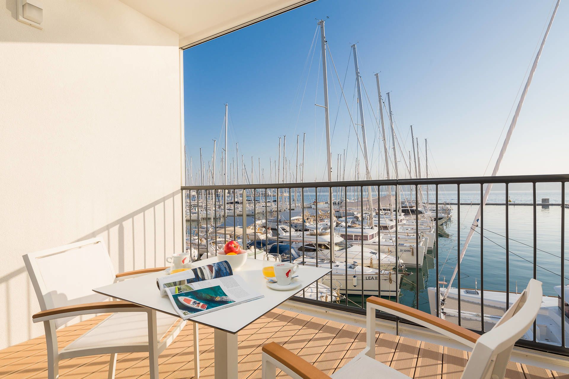 En balkon med et bord dækket til to, med udsigt over en lystbådehavn fyldt med både.