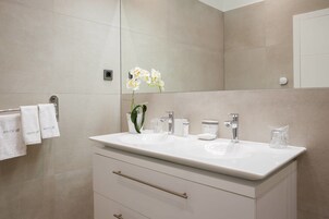 A modern bathroom with a white vanity, two sinks, a mirror, and a towel rack with white towels.