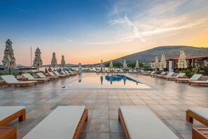 A poolside area with lounge chairs and umbrellas, a clear sky, and a mountain in the background. - Marina Baotić Apartments (Seget)