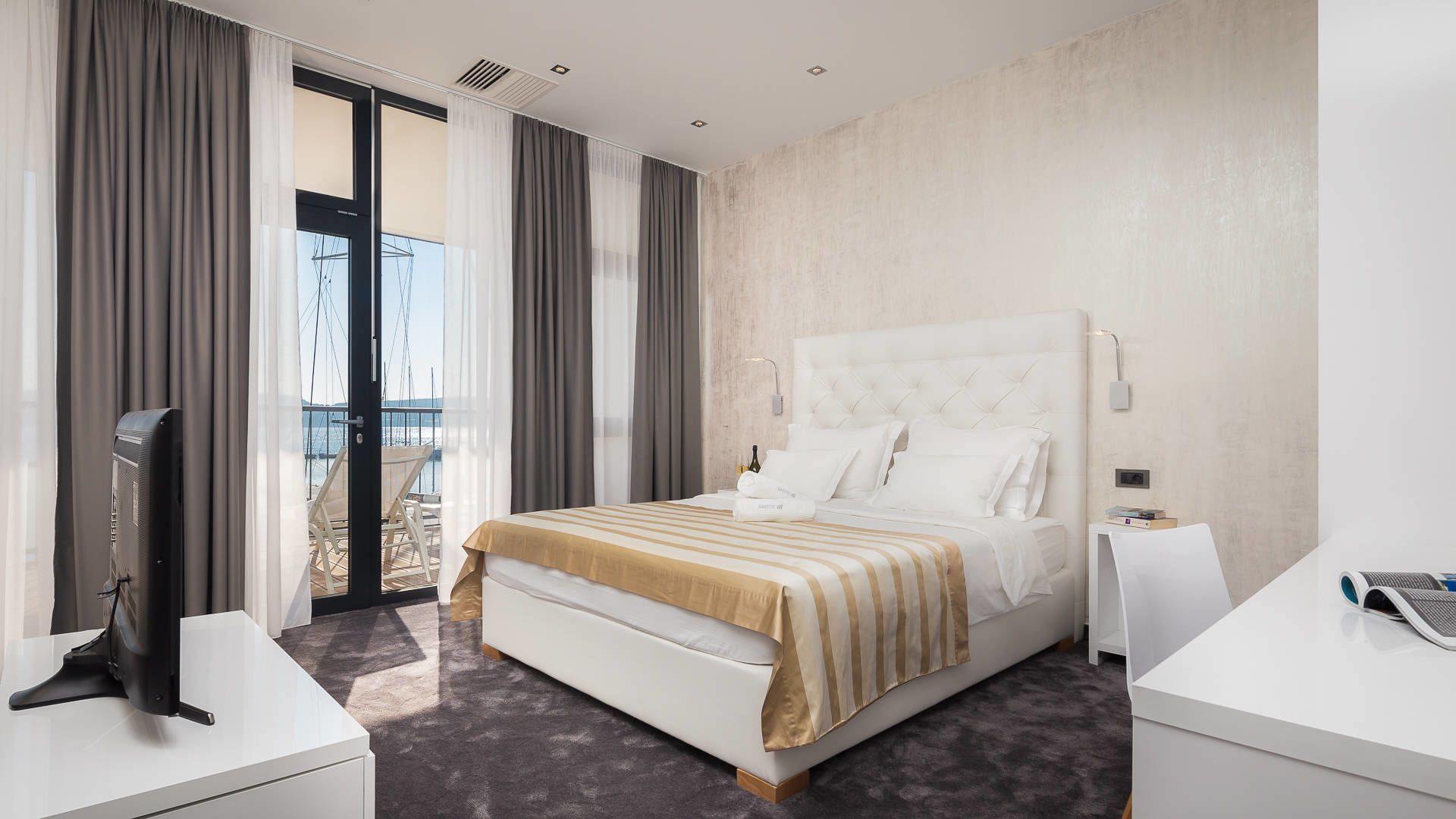A modern hotel room with a large bed, a flat-screen TV, and a balcony with a view of the sea.