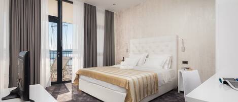 A modern hotel room with a large bed, a flat-screen TV, and a balcony with a view of the sea.